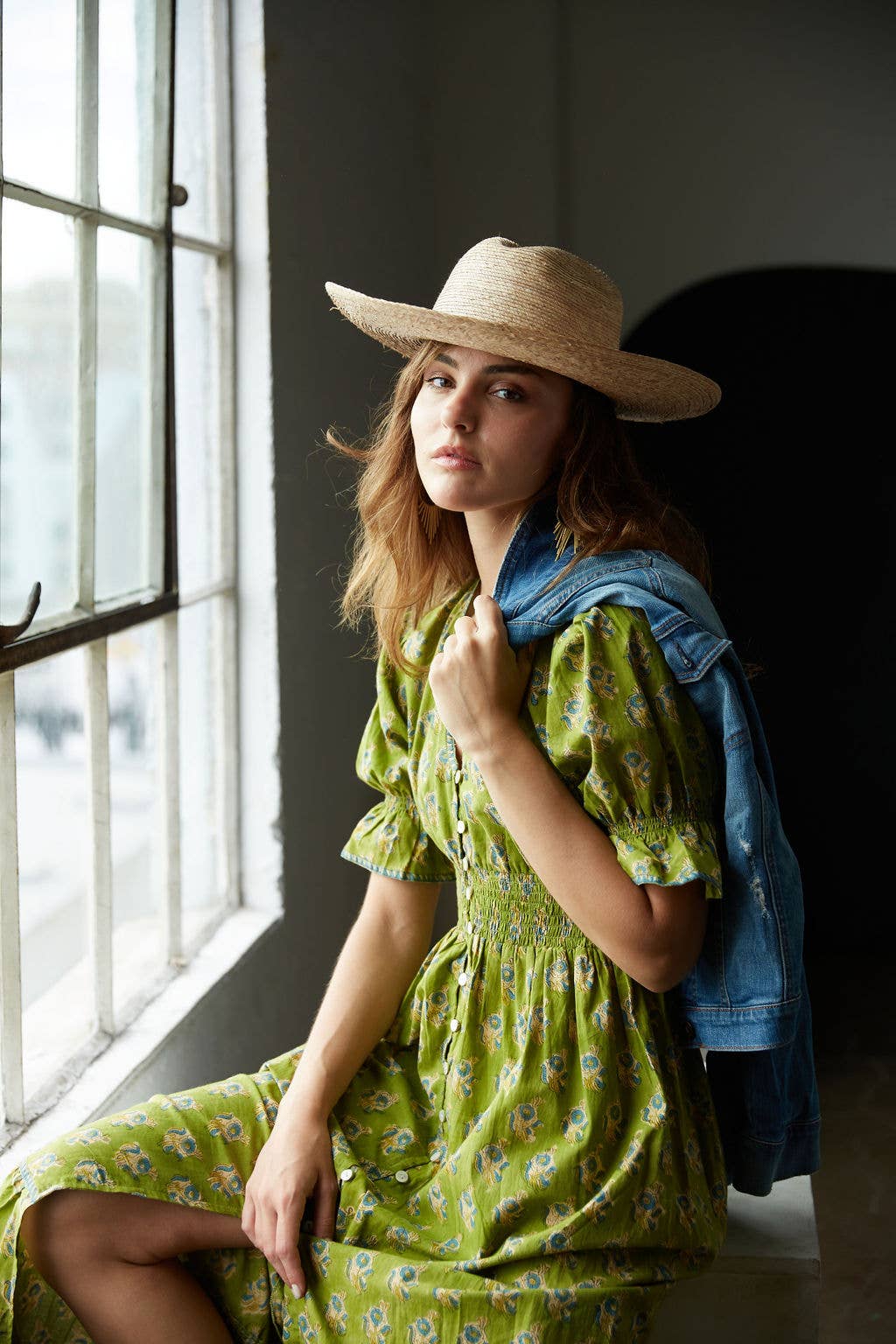 Woman in a green dress and straw hat sitting by a window