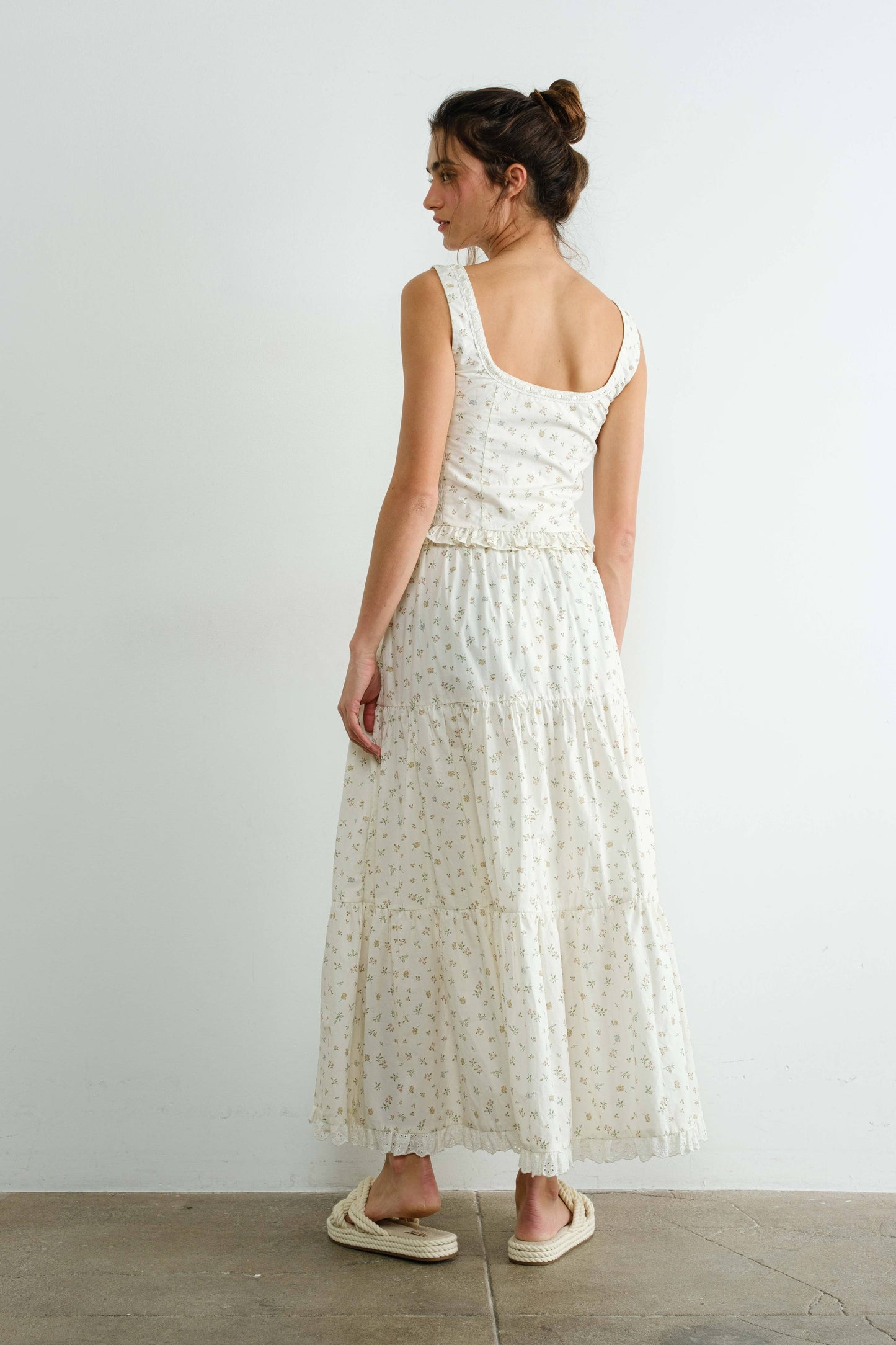 Woman wearing a white floral dress standing against a plain white wall.