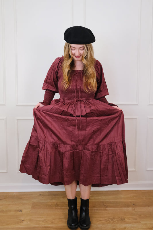 White woman in mulberry colored long-sleeve maxi dress and black french beret