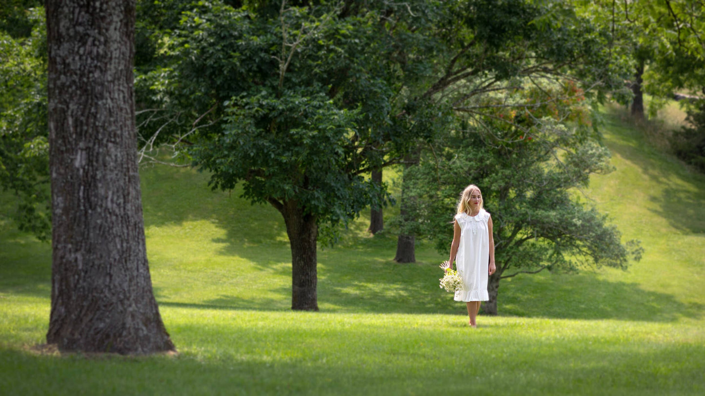 Woman in a white dress standing in a park with trees and grass.