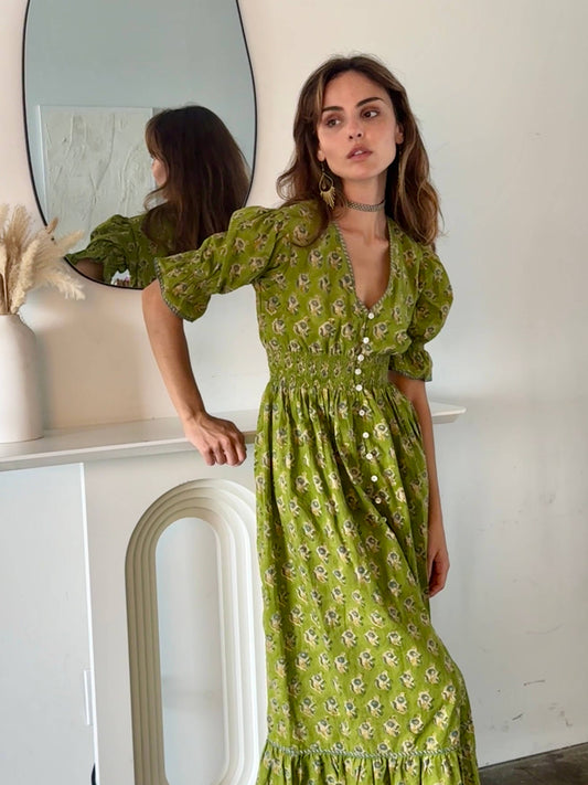 Woman in a green floral dress standing in front of a mirror.