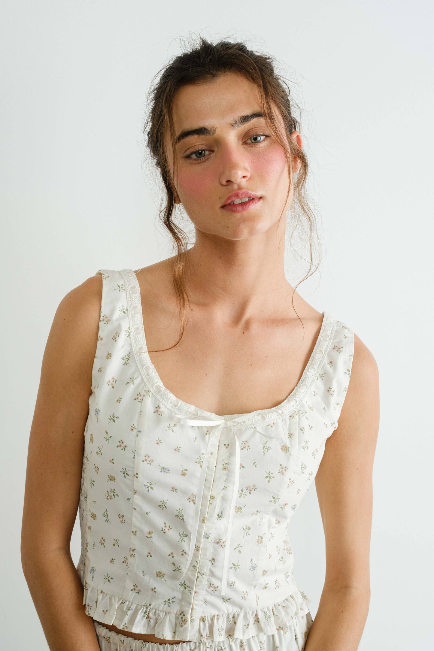 Woman wearing a white sleeveless top with a subtle pattern against a plain background