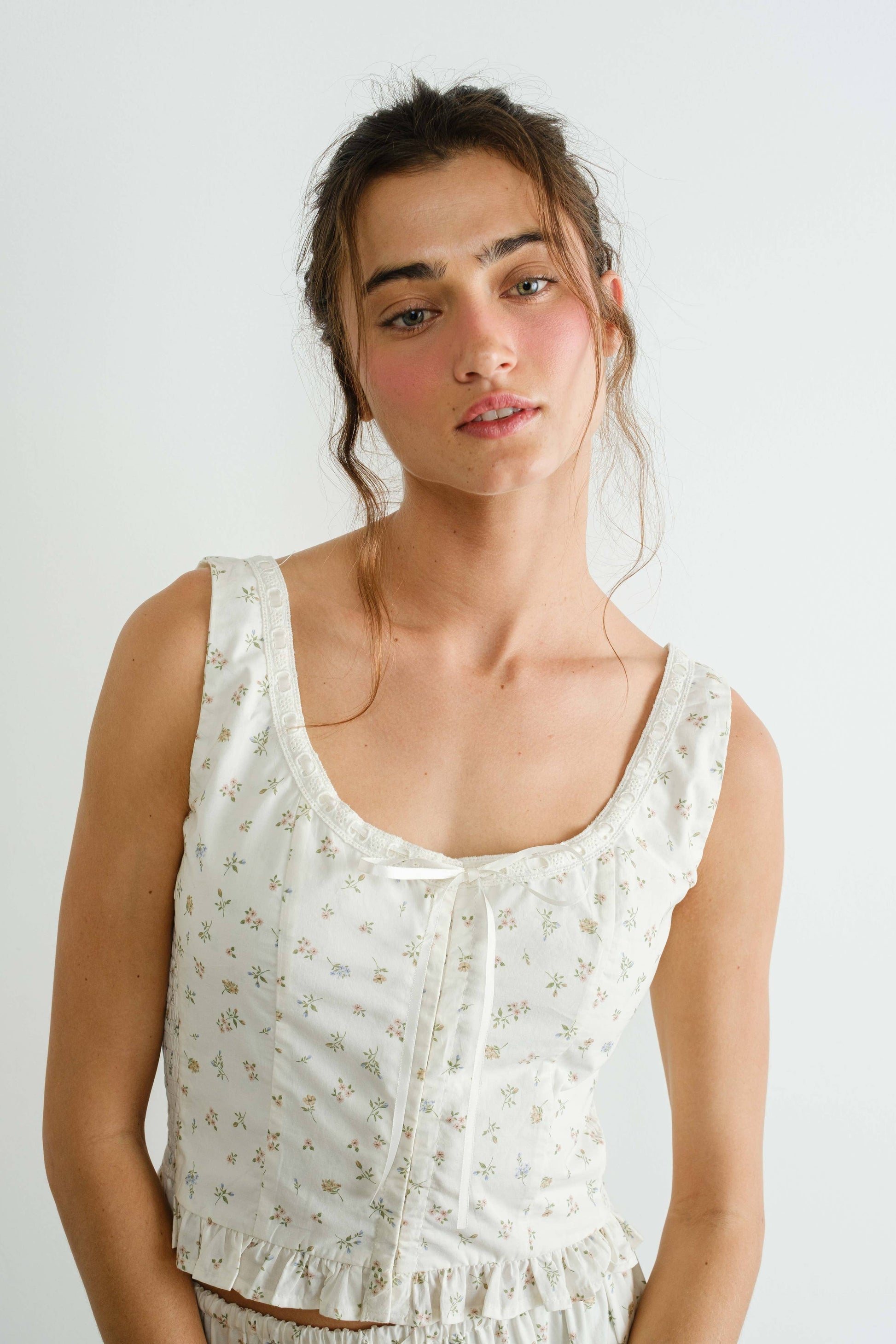 Woman wearing a white sleeveless top with a subtle pattern against a plain background