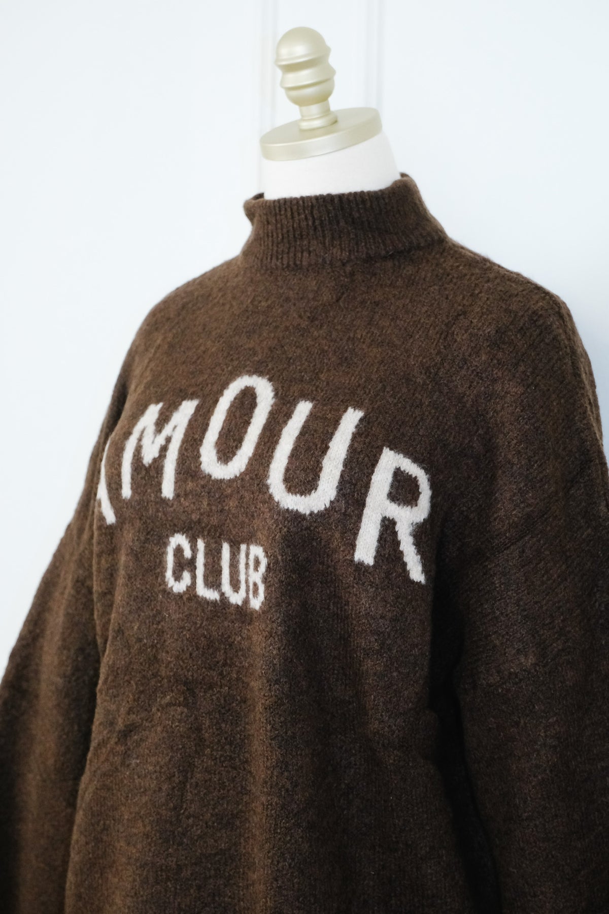 A brown fuzzy knit mock-neck sweater with 'IMOUR CLUB' knitted in white across the chest, displayed on a cream dress form mannequin against a white background.