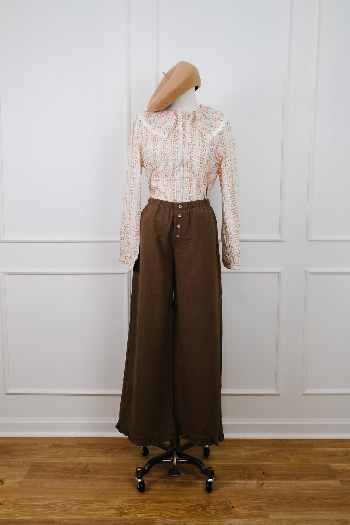 A two-piece clothing set displayed on a mannequin, featuring a long-sleeve button-up shirt with a beige and orange patterned tweed-like fabric, paired with high-waisted, wide-leg brown trousers with front buttons.