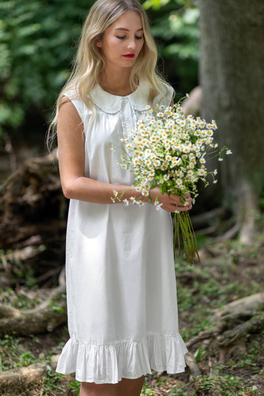 Woman in a white dress holding flowers in a forest setting