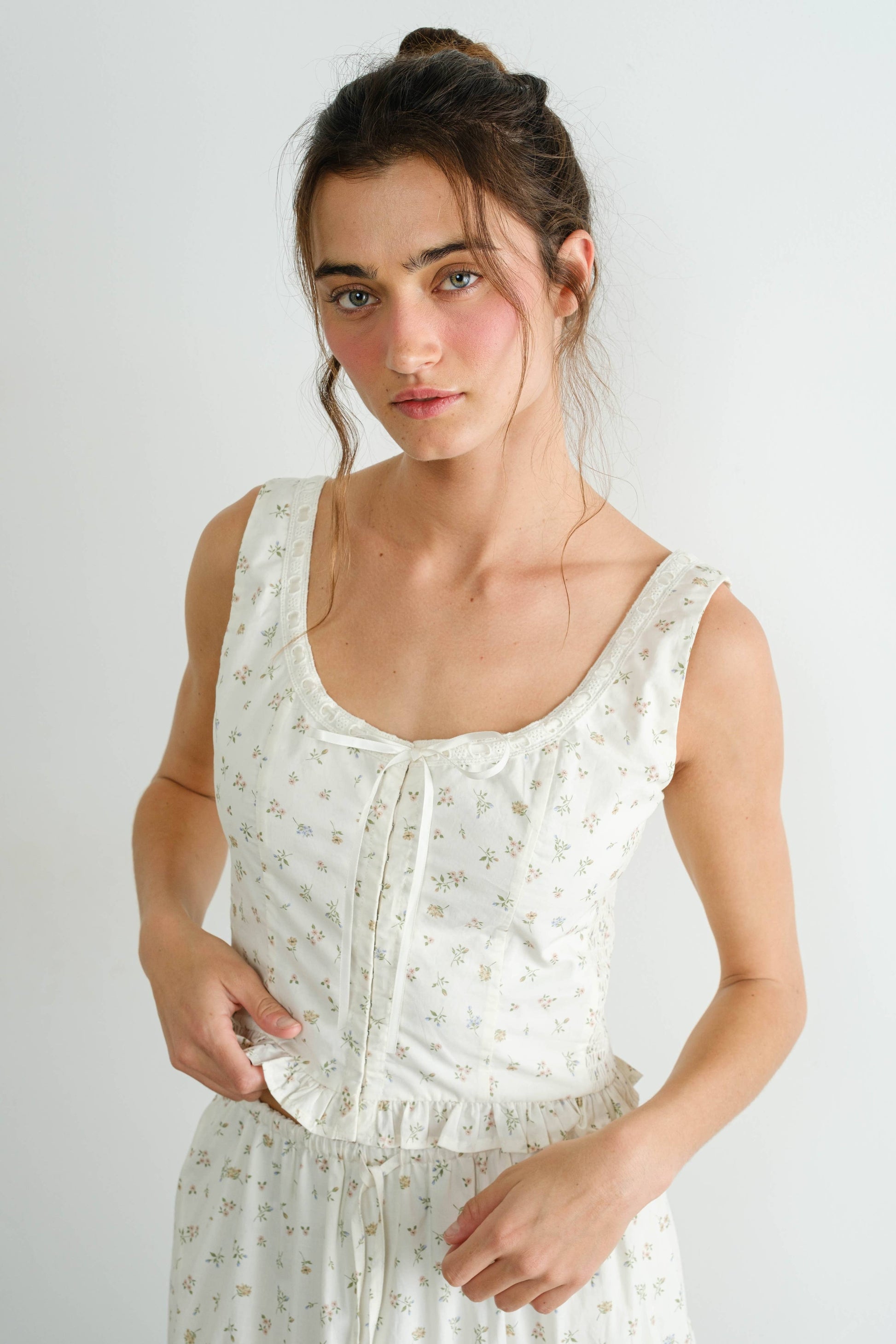 Woman wearing a white sleeveless top with a subtle pattern on a plain background