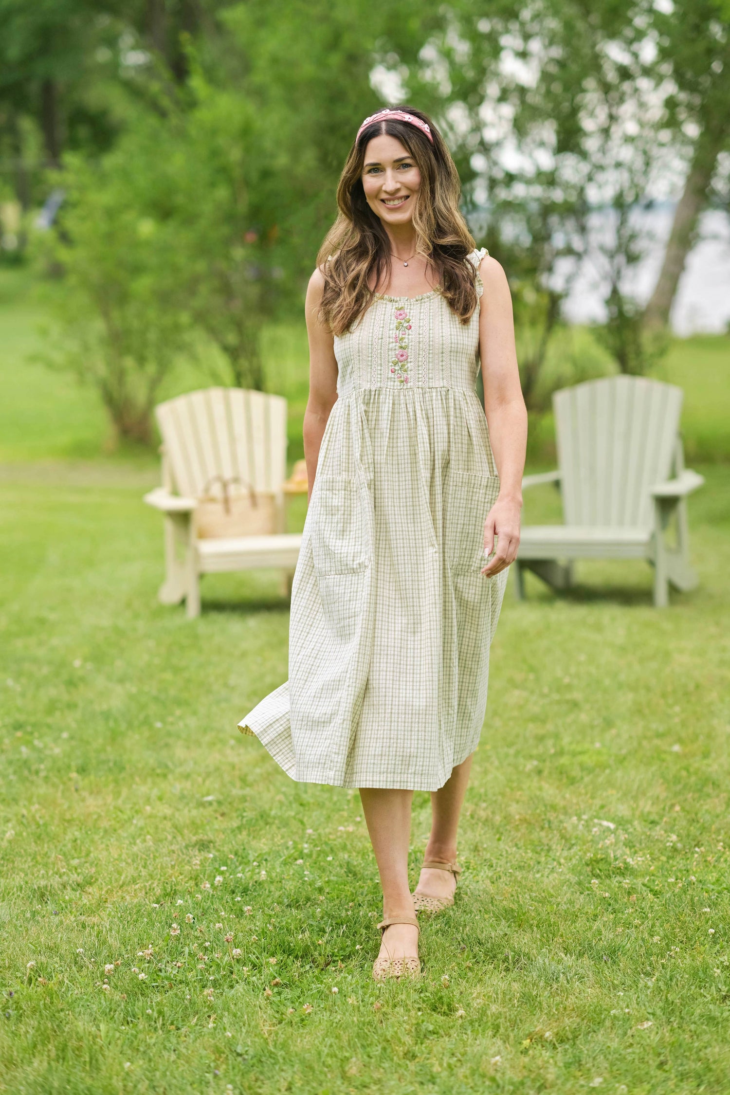 Woman in a white dress standing in a grassy outdoor area with chairs in the background.