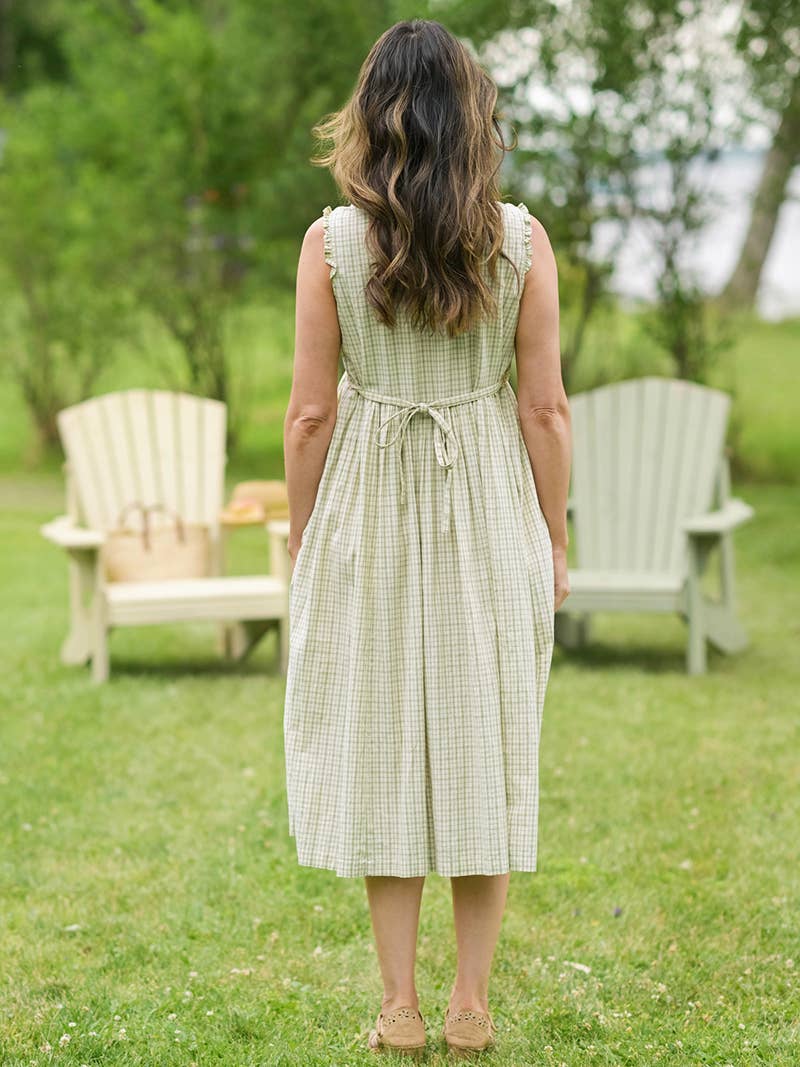 Woman in a green checkered dress standing in a grassy area with chairs in the background