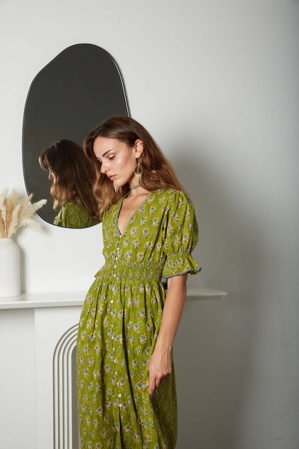Woman in a green floral dress standing in front of a mirror.